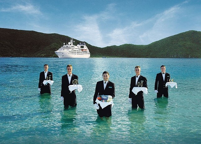 five waiters in the water with boat in the background