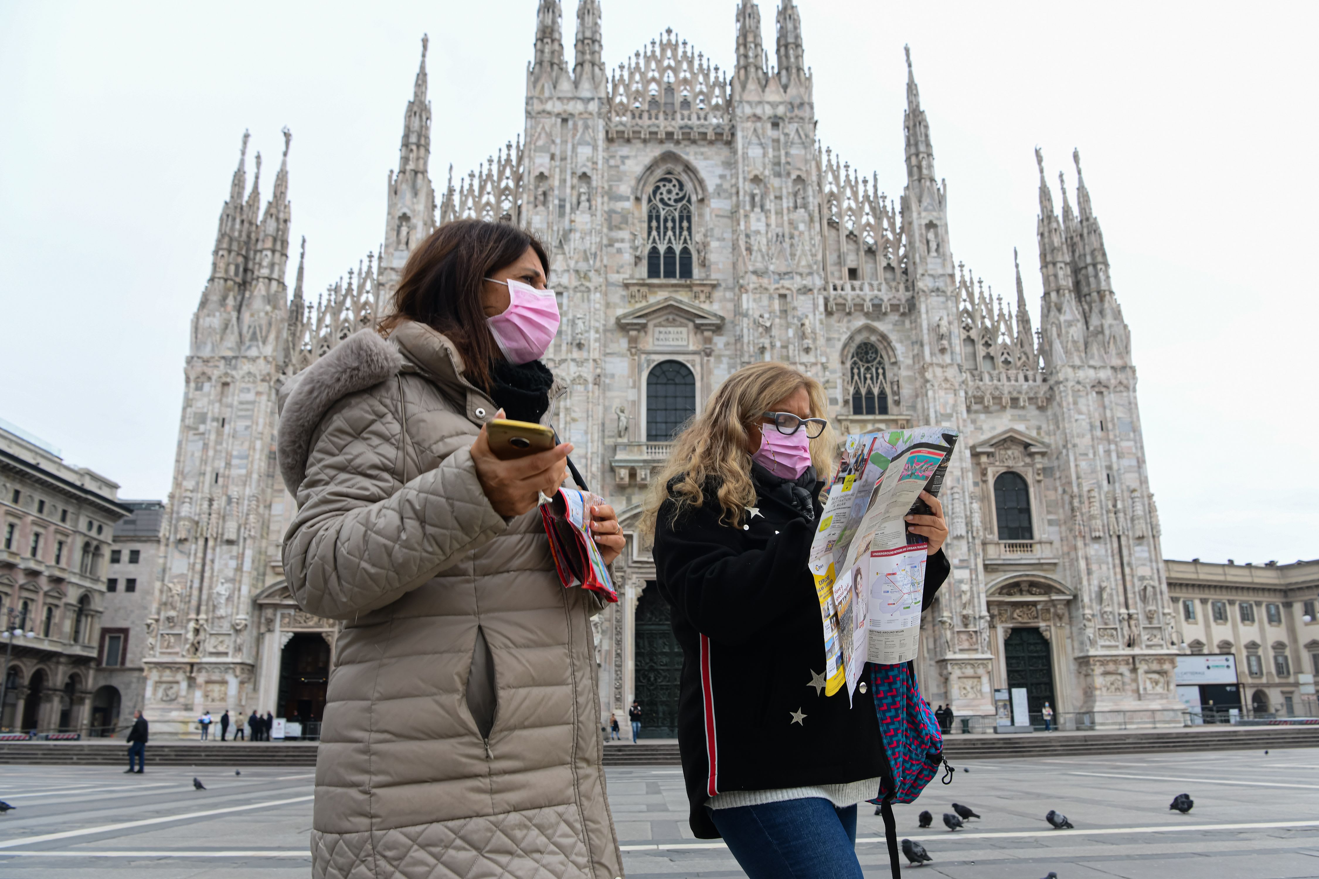 two women wear masks and stand in front of church