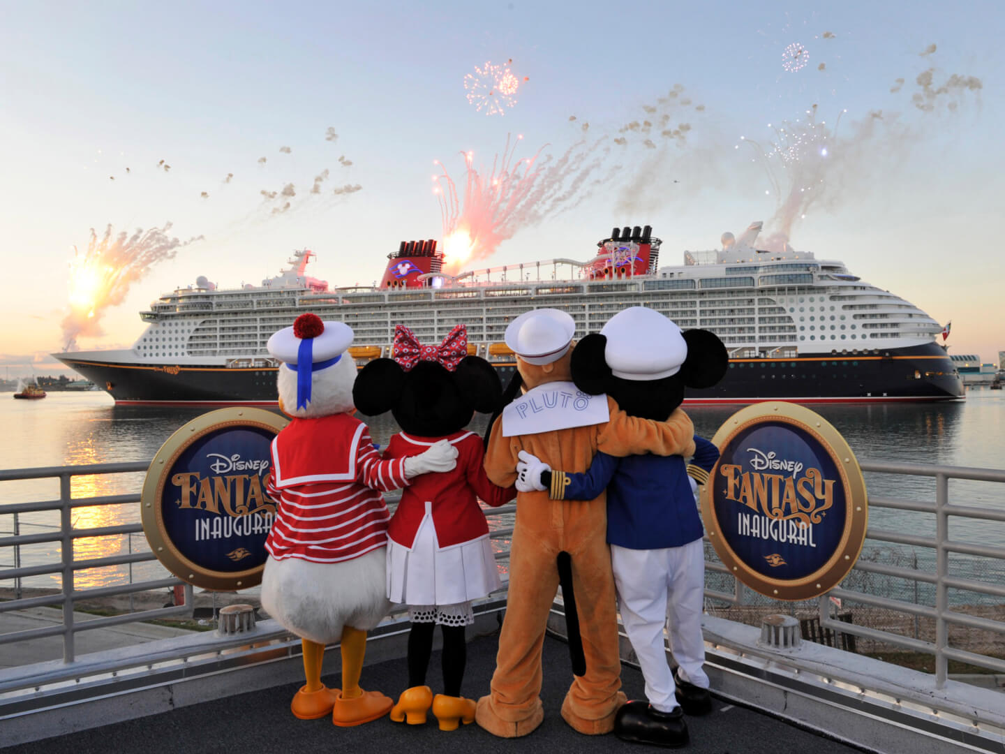 four Disney characters embrace as they watch a Disney cruise ship sail by